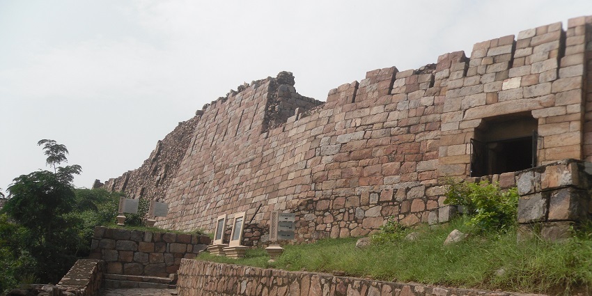 A picture of a fort wall showcasing the ancient architecture used to build it with a garden nearby