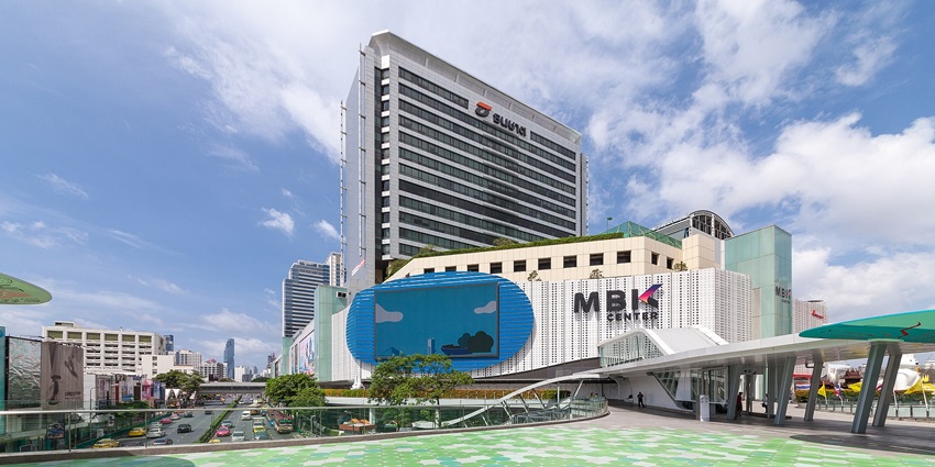 A mindblowing front shot of the MBK Shopping Centre with cars passing by in Bangkok.