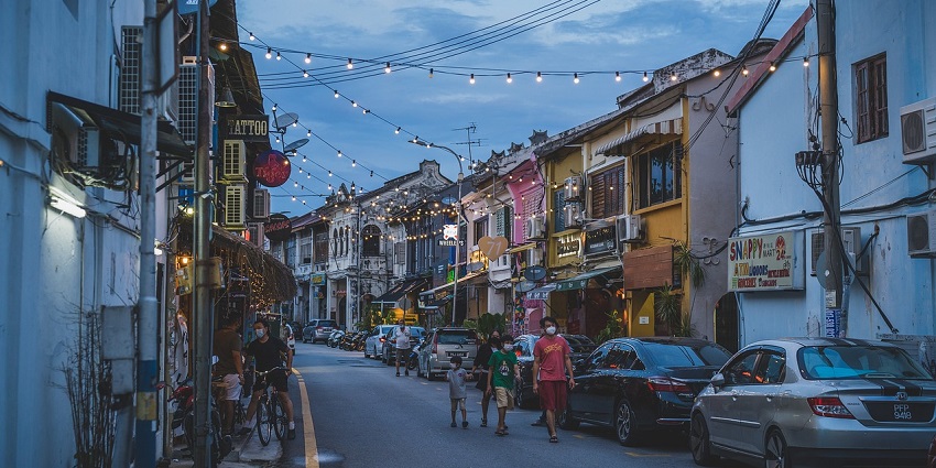 Street at sunset with people walking along, featuring a warm glow over the town.