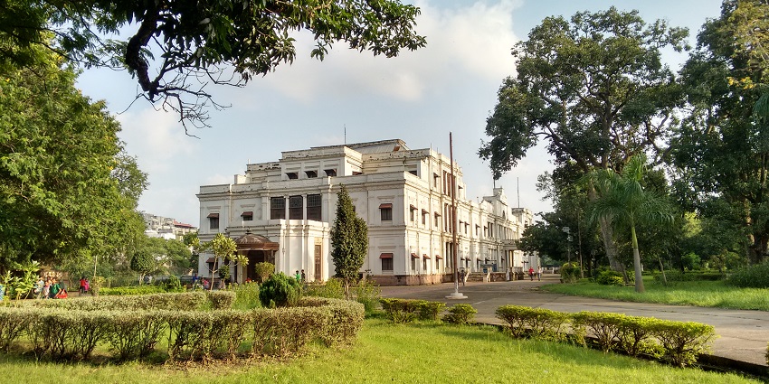 Large building with many windows and lush greenery around, similar to Madhav Vilas Palace