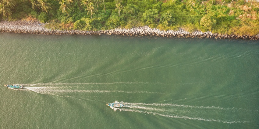 A bird’s eye view of azure waters with speeding boats and surrounded by greenery.