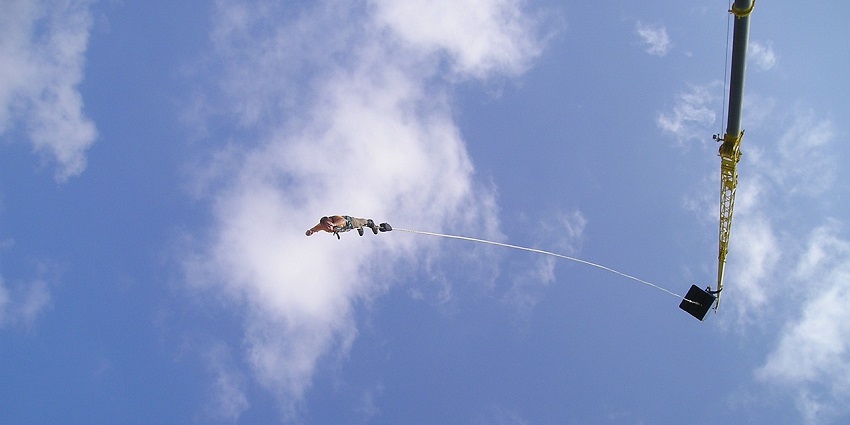 Shot of bungee jumping amidst the process, a tourist tied to the rope with blue sky in the background
