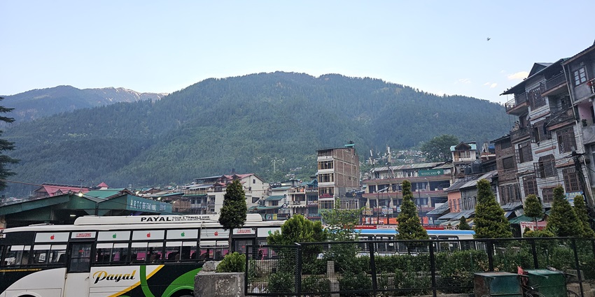 Image of Manali city with houses and hotels and lush green mountain in the background.