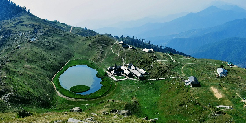 Beautiful view of a small lake in a valley in Mandi, under clear blue sky and mountains around