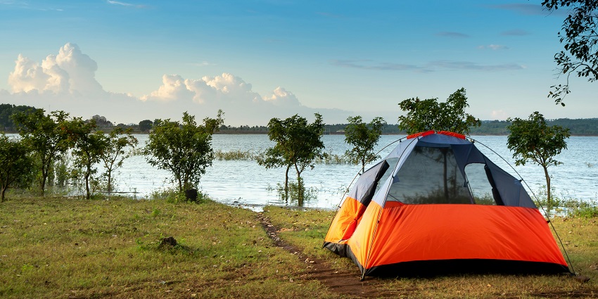 A mesmerising view of an orange tent on a green grassland with a waterbody on the side.