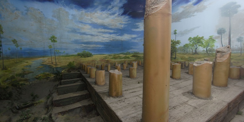 A colonnade of tall and broken columns with a painted wall forms the exterior design.