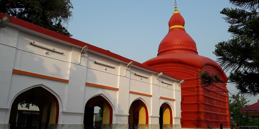 Matabari Temple in Tripura, a sacred site with a white dome and red trim, surrounded by greenery.