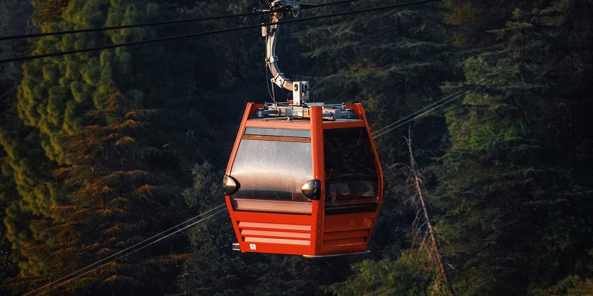 Image of a red cable car in the middle of a forest in McLeod Ganj surrounded by green mountains