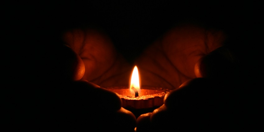 A close-up image of a person's cupped hands gently holding a small tealight candle.
