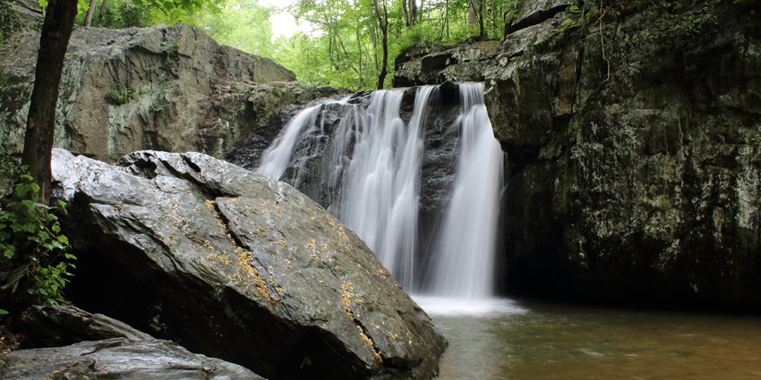 The picture of the mesmerising view of the Menal Waterfalls surrounded by green trees.