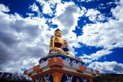 A breathtaking view of a statue of Buddha on a cliff under dense clouds during the day.