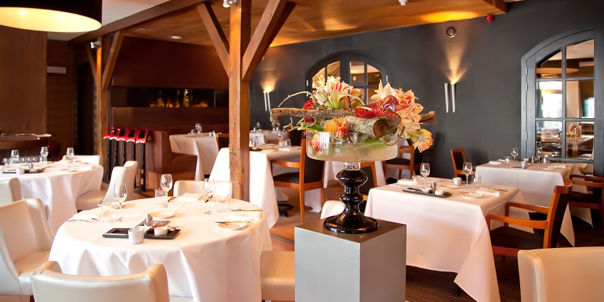 View of a elegant restaurant , with white clothed tables and bouquets
