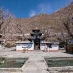 The Muktinath Temple in Nepal with mountains in the background and brown trees.