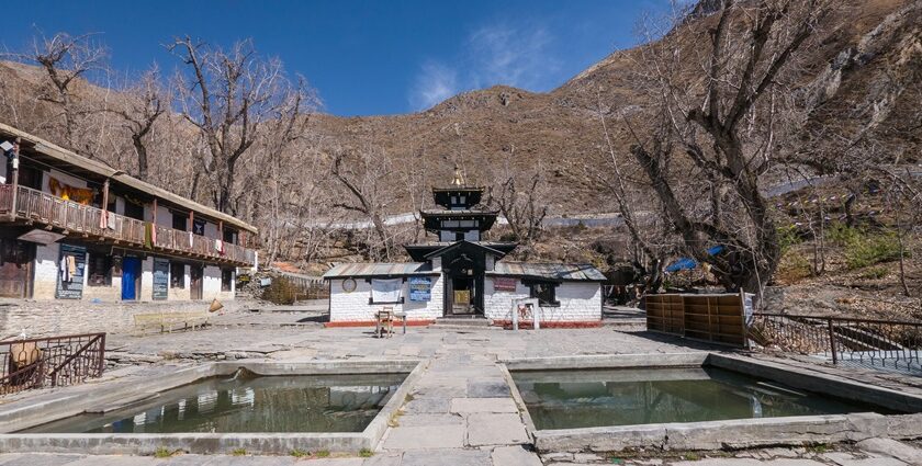 The Muktinath Temple in Nepal with mountains in the background and brown trees.