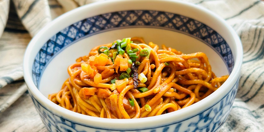 Image of a bowl of noodles with spring onion on top served in a bowl hot and dry