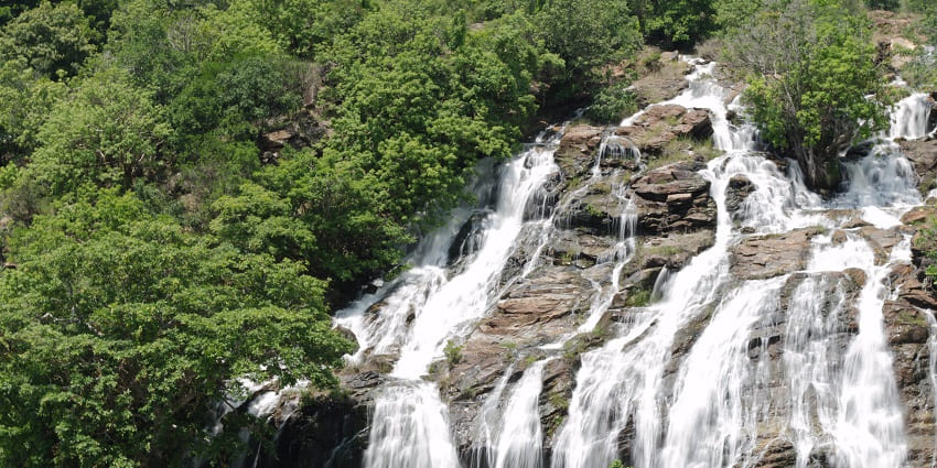 A large waterfall cascading down rocky cliffs, surrounded by lush greenery in Karnataka
