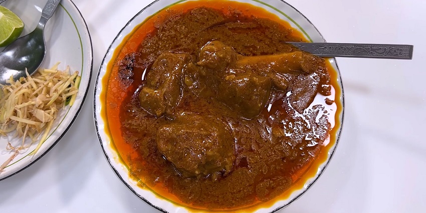 A steaming bowl of Nihari served with naan, showcasing rich spices and tender meat