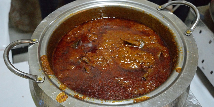 A mouth-watering view of a big utensil served with mutton rogan josh on a table.
