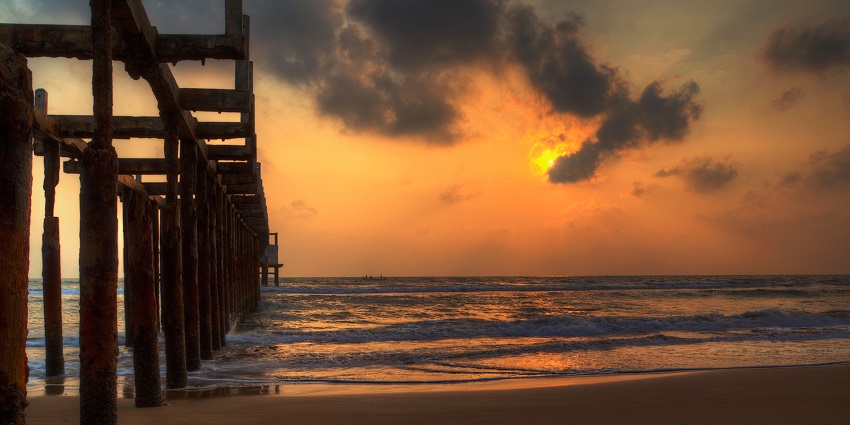 A picture of a beach taken at the stroke of sunset with the cloud turning orange in colour