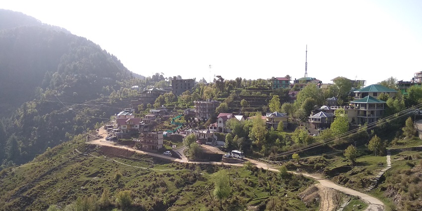 Picturesque view of Naddi Village with traditional houses, lush greenery, and distant mountains, a famous tourist place near Bhagsunag Temple