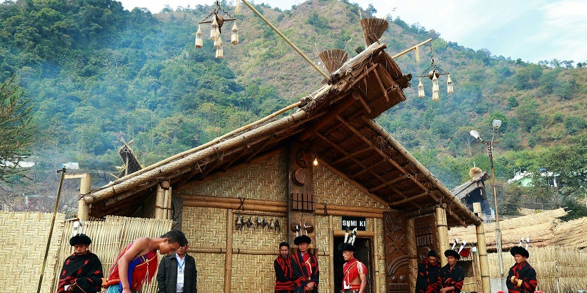 A diverse group of people gathered outside a rustic hut, smiling and enjoying.