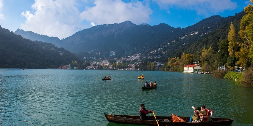 Image of serene view of Nainital Lake surrounded by lush hills and clear blue skies.
