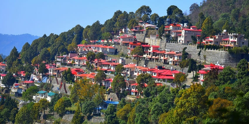 Scenic view of Nainital's serene lake surrounded by lush green hills and charming cottages.
