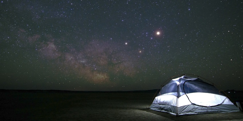 A tent illuminated under a clear night sky filled with bright stars and constellations.