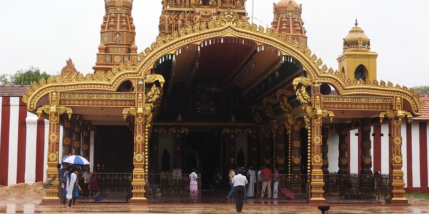 A stunning view of a temple with golden architecture and people in front during the day.