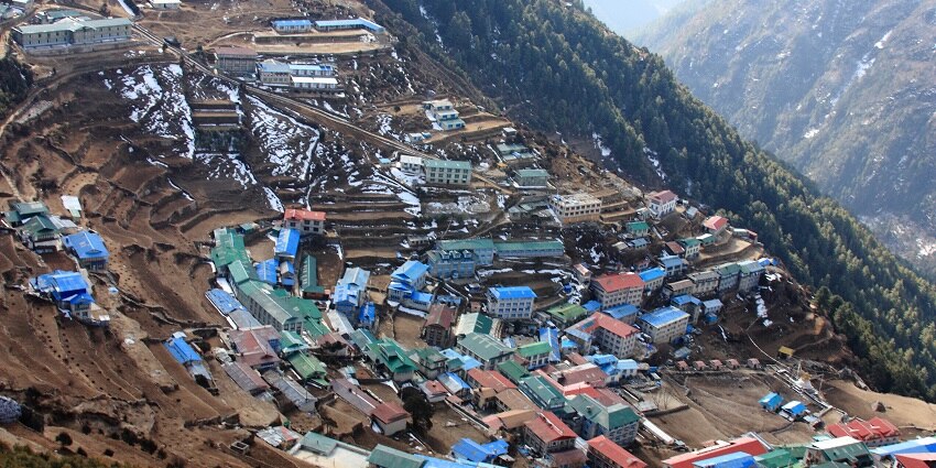 Namche Bazaar is nestled in the Himalayas, featuring traditional buildings and surrounding peaks