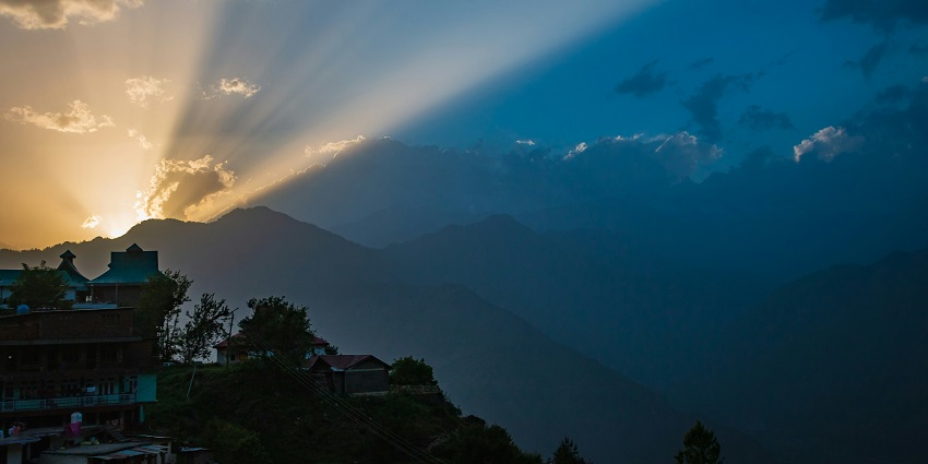 Snapshot of the sun hiding behind the clouds and the lush green hills to create an alluring atmosphere