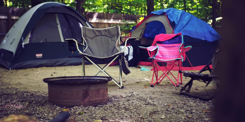 A breathtaking view of a dense forest with colourful chairs in front of assorted tents.