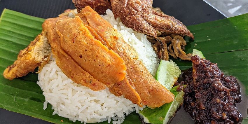 Nasi lemak served on a banana leaf with rice, fried anchovies, peanuts, and spicy sambal.