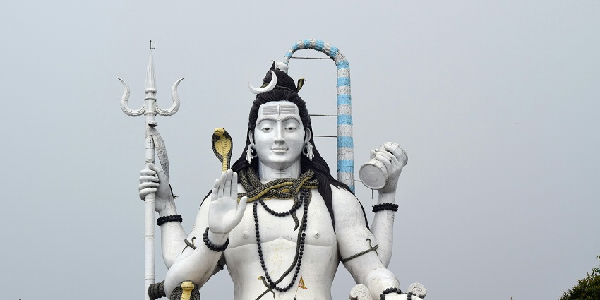 A picture of a tall statue of lord Shiva under a bright sky in their famous sitting position