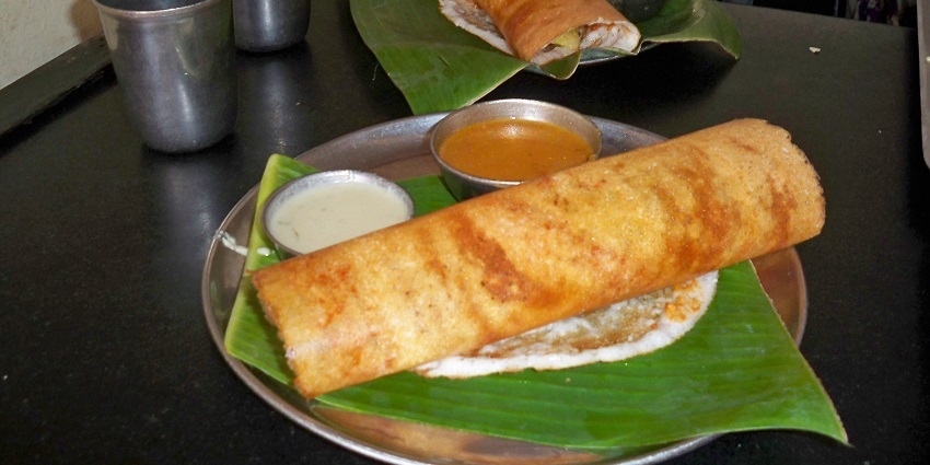 Dosa served on a wooden tray with a banana leaf, one of the best foods in Bharuch