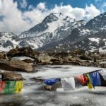 Buddhist flag hanging by a creek, near snow mountains - Places to visit in Nepal in May.