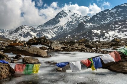 Buddhist flag hanging by a creek, near snow mountains - Places to visit in Nepal in May.