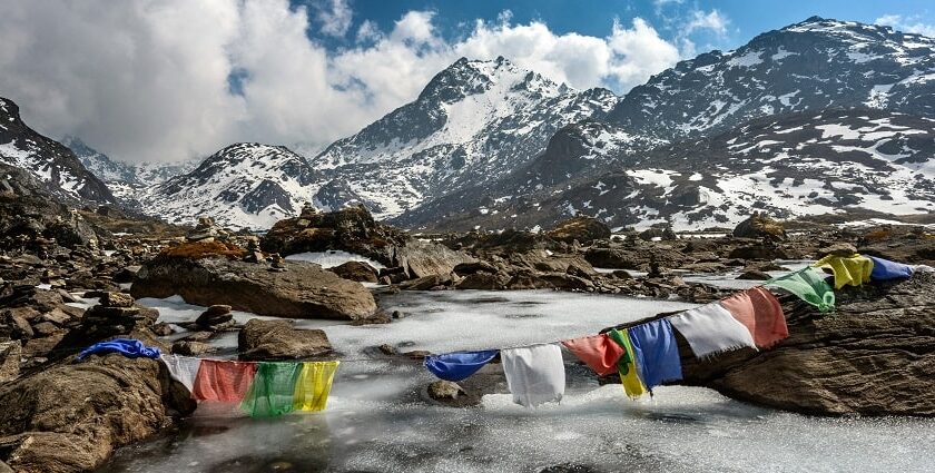 Buddhist flag hanging by a creek, near snow mountains - Places to visit in Nepal in May.