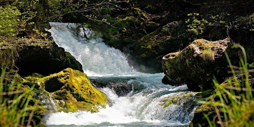Roaring water stream at Neugal Khad, surrounded by majestic mountains and lush greenery