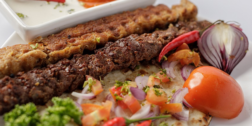 Kebabs, skewered pieces of marinated meat, are served with flatbread and fresh vegetables.