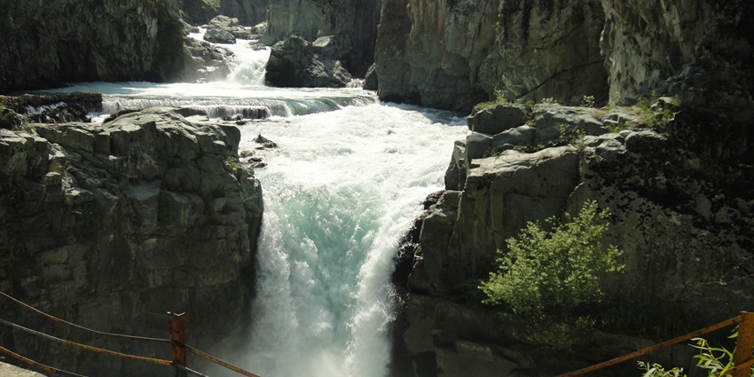 The beautiful waterfall cascades down a rocky cliff surrounded by lush green foliage.