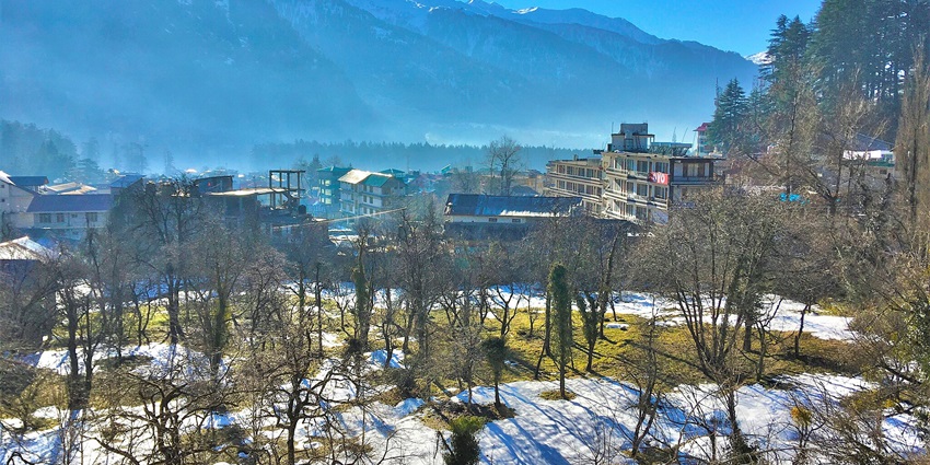 Image of old Manali covered in snow under clear blue sky and sun shining.