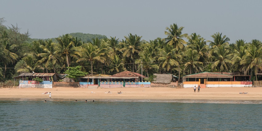 A panoramic vista of placid waves and pristine white sands decked with palm trees.