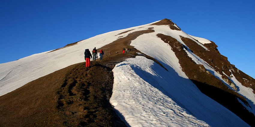 Trekkers on the snowy trail to Sar Pass, surrounded by snow and majestic mountain peaks