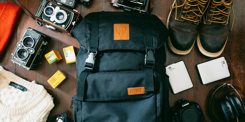 Packing high-angle shot of a black bag, cameras, a portable HDD, and black leather lace-up boots.