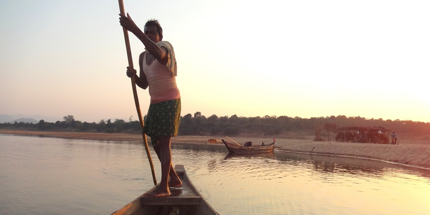 Man riding a boat at Mahanadi Riverfront near Deulajhari Hot Spring with forest area in the background.
