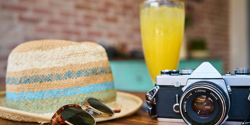 Image of a grey and black camera with a hat and juice on the side - travelling essentials