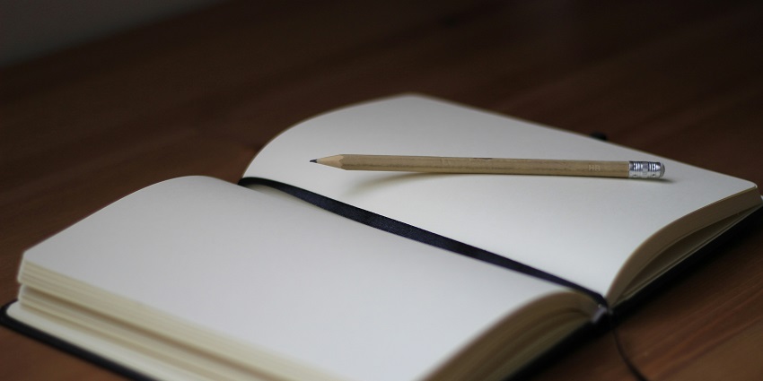 A selectively focused view of a white notebook with a brown pencil sitting on it.