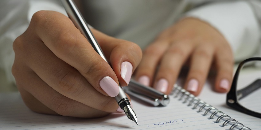 An amazing view of a woman’s hand writing on a piece of paper with a golden pen.