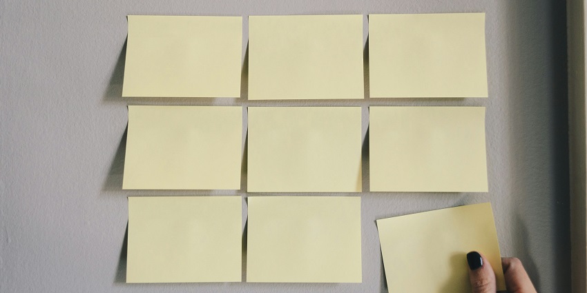 A frontal view of a few sticky notes on a plain white surface with a hand holding one.
